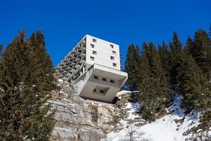 Ein modernes Gebäude mit einem markanten, vorspringenden Design, umgeben von einem Waldgebiet.