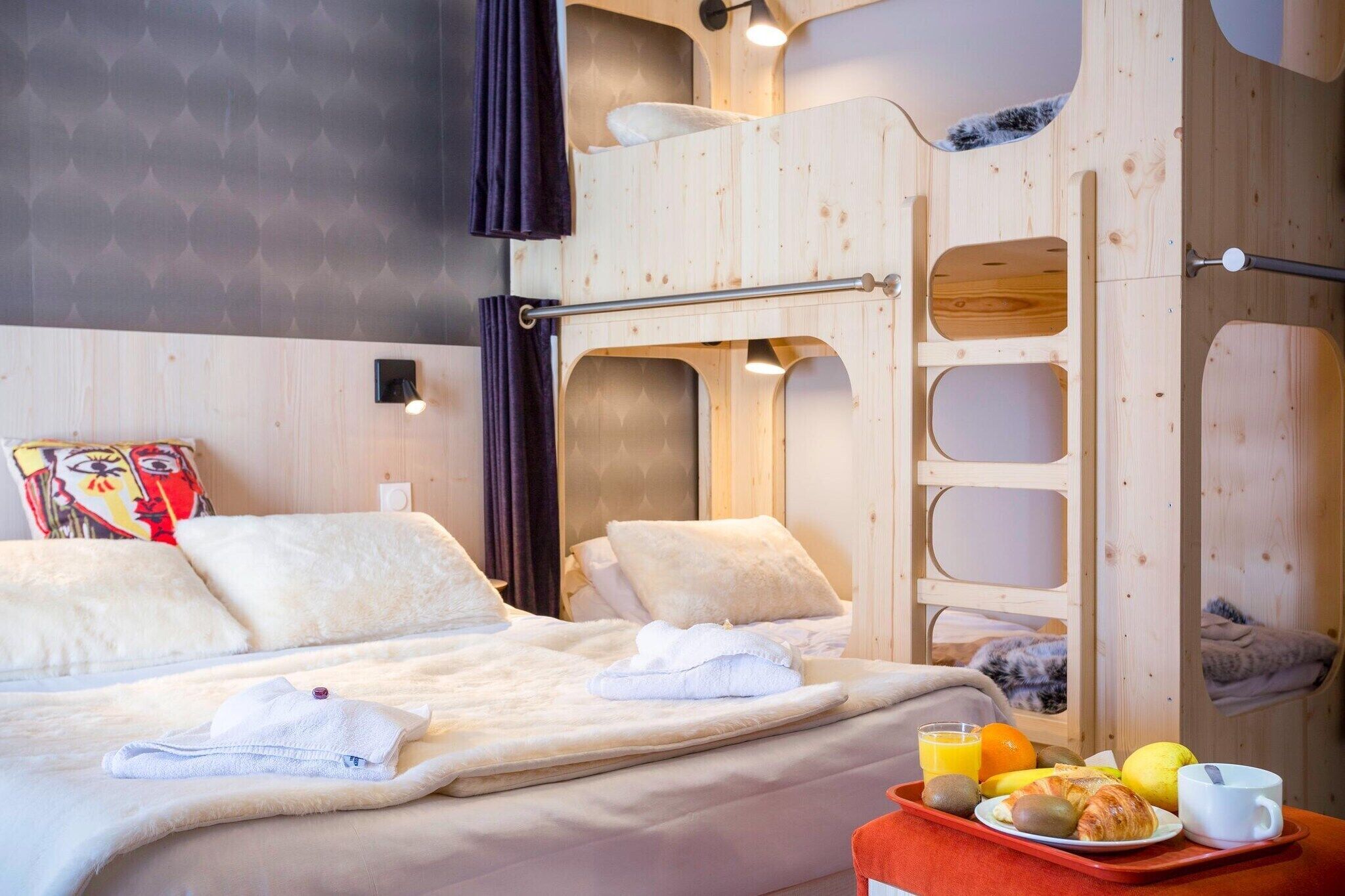 A room with a bunk bed, a bedside table with breakfast items, and a wall with a geometric pattern.