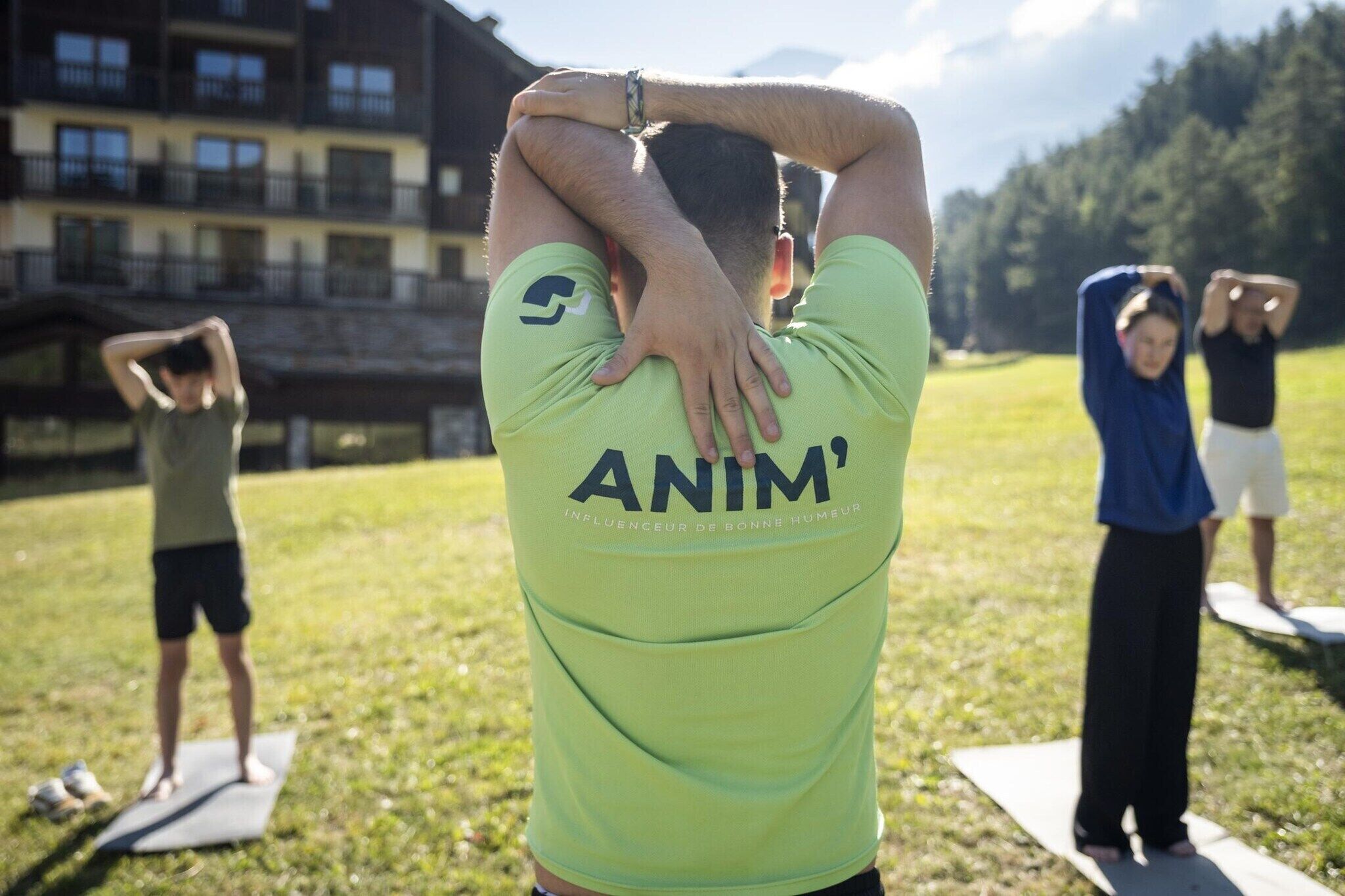 A person in a green shirt with 'ANIM' on the back, standing on a yoga mat outdoors.