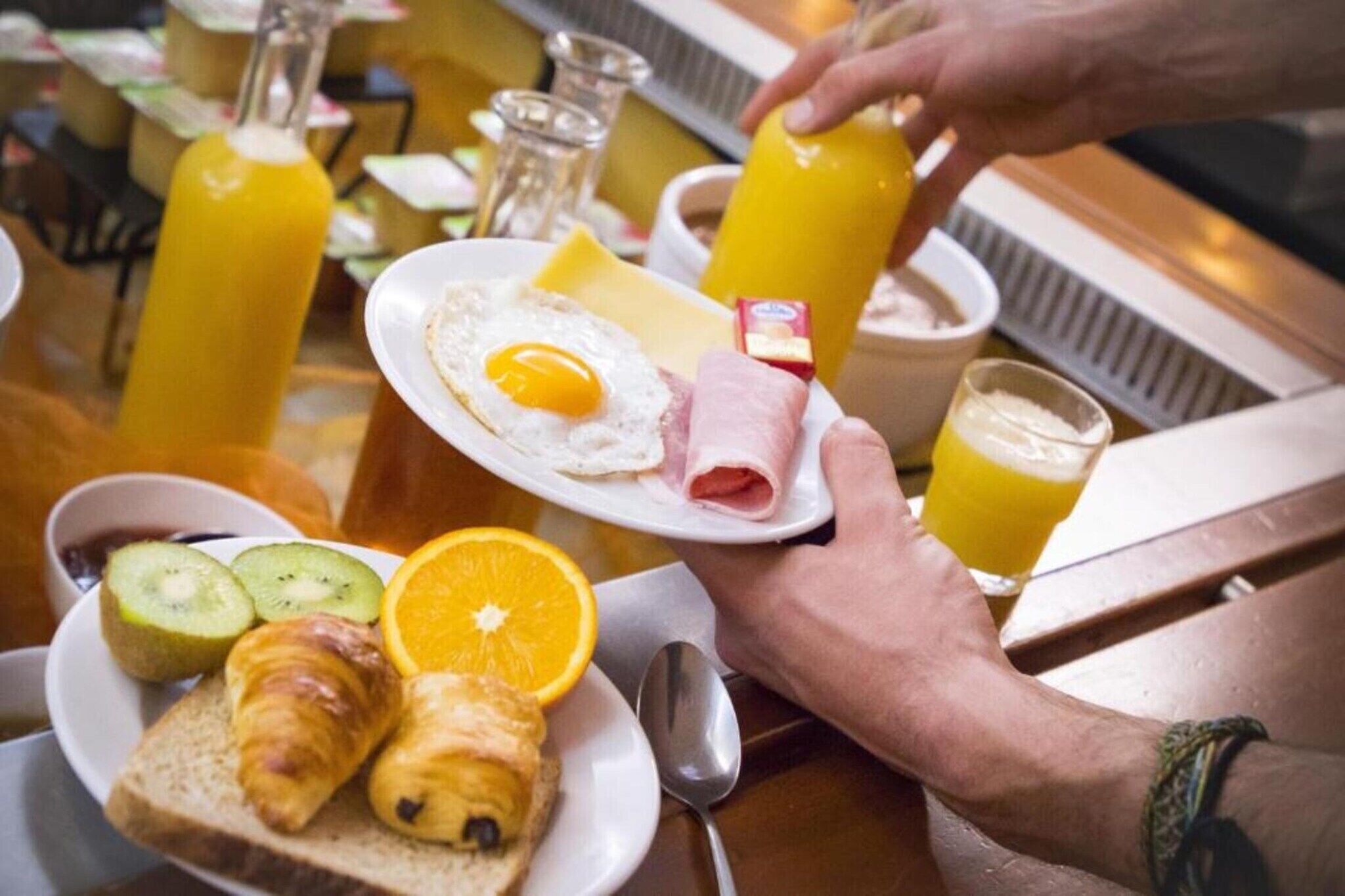 Une table mise pour le petit-déjeuner avec une assiette d’œufs, de jambon et de croissants, accompagnée d’un verre de jus d’orange et d’une carafe de jus d’orange.