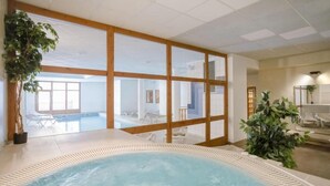 En indendørs swimmingpool med træterrasse, store vinduer og opholdsområde indendørs.