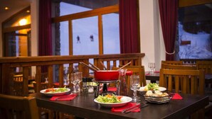Spisebord dækket med tallerkener, glas og en rød fonduegryde, med udsigt til et sneklædt landskab gennem store vinduer.