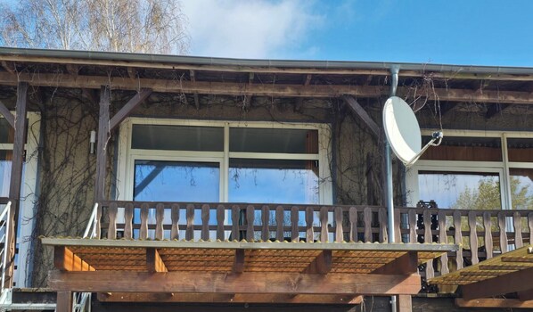 Ein Holzbalkon mit Geländer, Satellitenschüssel und einem großen Fenster.