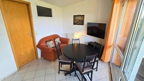 A compact living space with a sofa, a dining table, chairs, a television, and a door. - Mobile Home im Ferienpark mit Seezugang (Dabel)