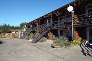 A building with a staircase leading to a balcony, surrounded by potted plants and a clear sky.