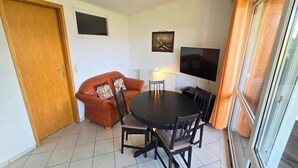 A compact living space with a sofa, a dining table, chairs, a television, and a door. - Mobile Home im Ferienpark mit Seezugang (Dabel)