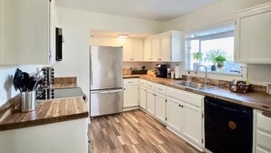 A modern kitchen with white cabinets, a stainless steel refrigerator, wooden countertops, and a dishwasher. - Cozy Craftsman Home by 6th Ave. Entire home in Tacoma, Washington (Tacoma)