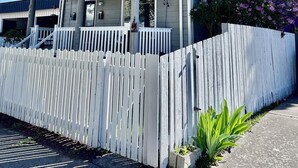 A two-story house with a porch, white picket fence, and a small garden with purple flowers. - Cozy Craftsman Home by 6th Ave. Entire home in Tacoma, Washington (Tacoma)