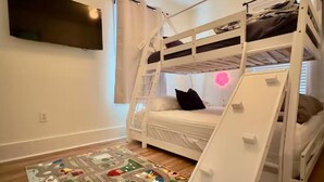 A bunk bed room with a TV mounted on the wall, a window with curtains, and a play mat on the floor. - Cozy Craftsman Home by 6th Ave. Entire home in Tacoma, Washington (Tacoma)