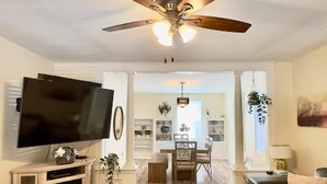 A living room with a flat-screen TV, ceiling fan, wooden flooring, and a dining area with a table and chairs. - Cozy Craftsman Home by 6th Ave. Entire home in Tacoma, Washington (Tacoma)