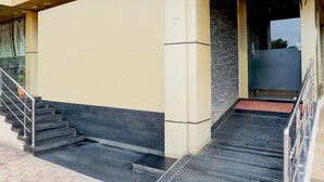 A set of black stairs leading to a door with a metal handrail, a beige wall, and a stone wall adjacent to the door. - Cosy Stays at Durg Near Railway Station (Durg)