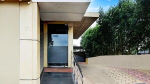 A building entrance with a ramp leading to a door, a tiled walkway, and a tree-lined area. - Cosy Stays at Durg Near Railway Station (Durg)