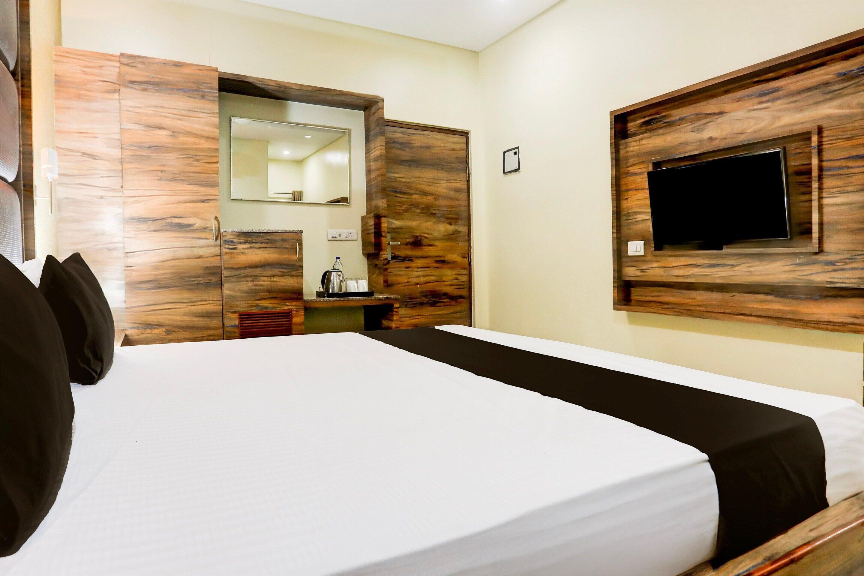 Une chambre d’hôtel avec un lit, une tête de lit en bois, un téléviseur fixé au mur et un miroir au-dessus du lit.