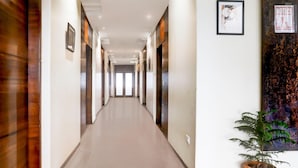 A hotel corridor with a polished floor, framed artwork on the walls, and a potted plant. - Cosy Stays at Durg Near Railway Station (Durg)