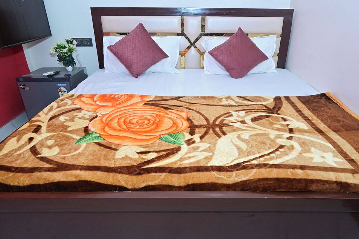 A bed with a floral bedspread, two pillows, a nightstand with a remote control, and a small plant.