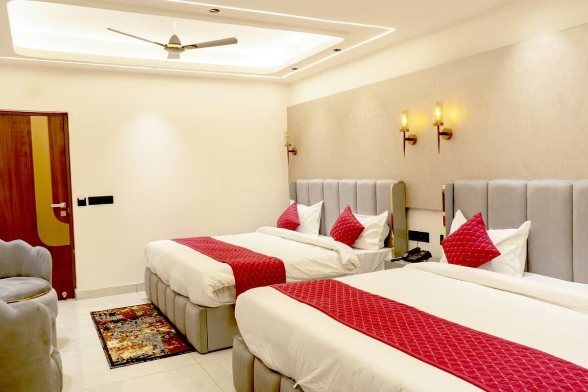 Ein Hotelzimmer mit zwei Betten, einem Deckenventilator, einem rot-weißen Teppich und einer Holztür.