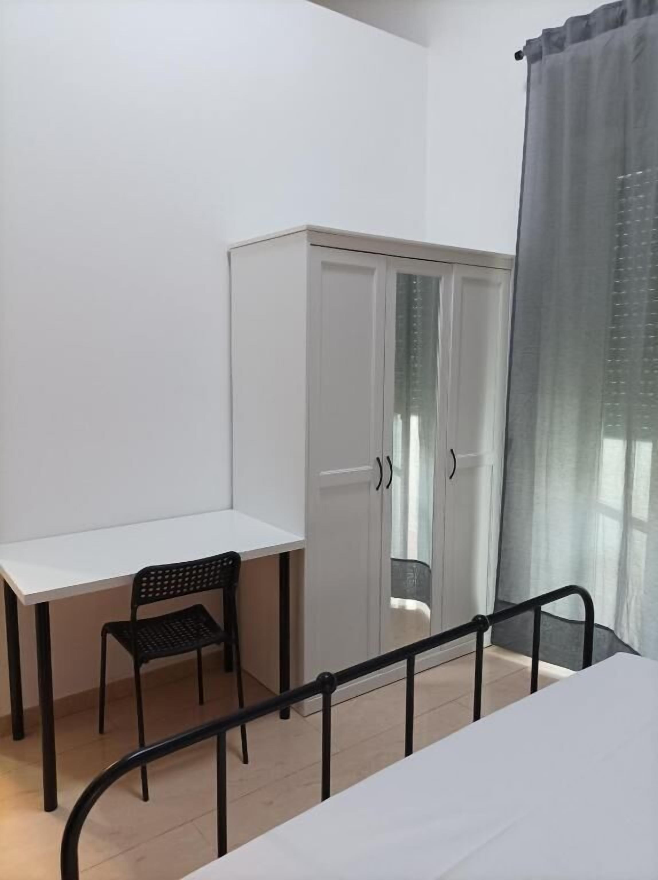 A room with a bed, a desk, a chair, and a wardrobe.