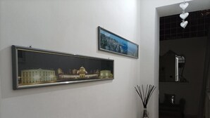 Ett rum med ett inramat fotografi av en byggnad, ett litet bord med en vas och en spegel på väggen.