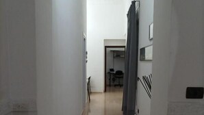 En smal hall med ett element på vänster sida, en stol och ett skrivbord i mitten och en gardin på höger sida.
