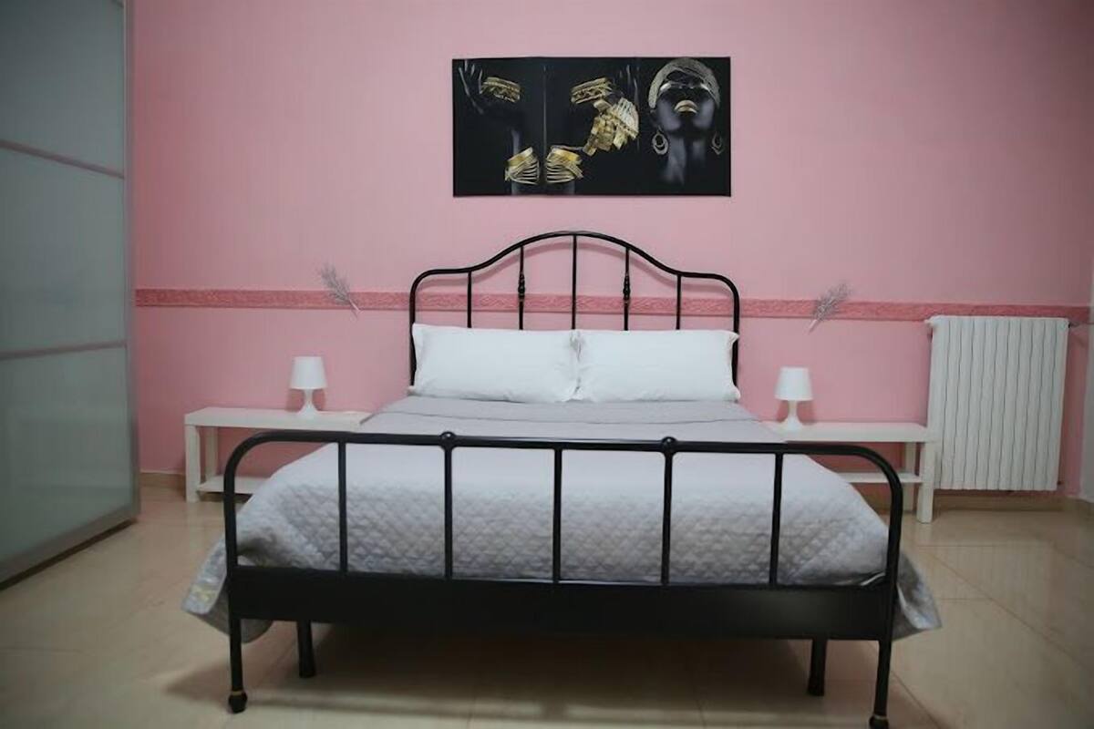 A bedroom with a bed, bedside tables, a radiator, and a wall-mounted artwork.