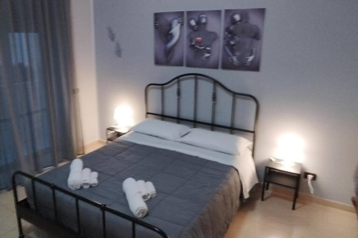 A single bed with a metal frame, two bedside tables with lamps, and a wall with three abstract art pieces.
