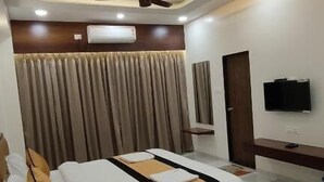 A modern hotel room with a large bed, a ceiling fan, a flat-screen TV, and a built-in air conditioning unit. - Hotel Grand Lushwood (Chhatrapati Sambhajinagar)