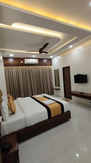 A modern hotel room with a large bed, a ceiling fan, a flat-screen TV, and a built-in air conditioning unit. - Hotel Grand Lushwood (Chhatrapati Sambhajinagar)