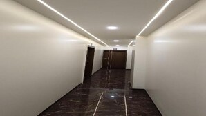 A corridor with white walls, a dark marble floor, and recessed lighting. - Hotel Grand Lushwood (Chhatrapati Sambhajinagar)