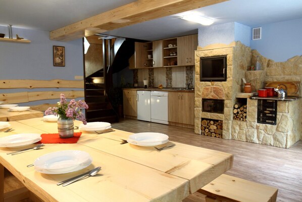 Un coin repas avec une table en bois dressée pour quatre personnes, une cuisine aux murs en pierre et un escalier menant à un autre niveau.