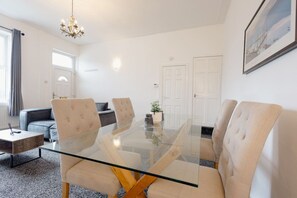 Ein moderner Konferenzraum mit Glastisch, gepolsterten Stühlen, einer Couch und einem Kronleuchter.