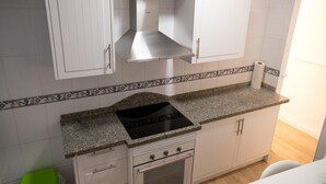 A kitchen with white cabinets, a granite countertop, a black stove, and a patterned backsplash. - Beautiful Apartment by the sea in Almeria (Almeria)