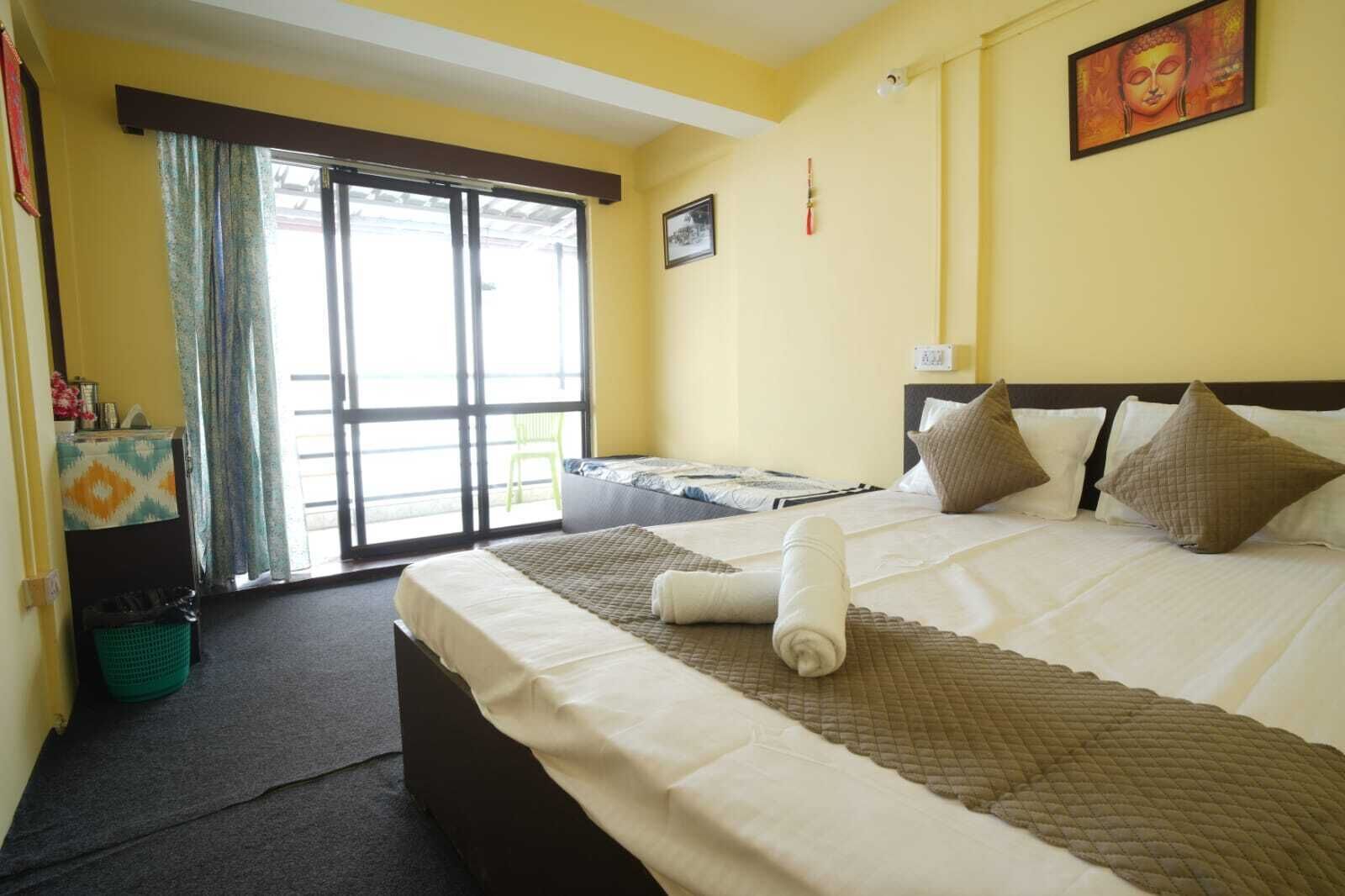 A hotel room with a bed, a window, a green chair, and a trash bin.