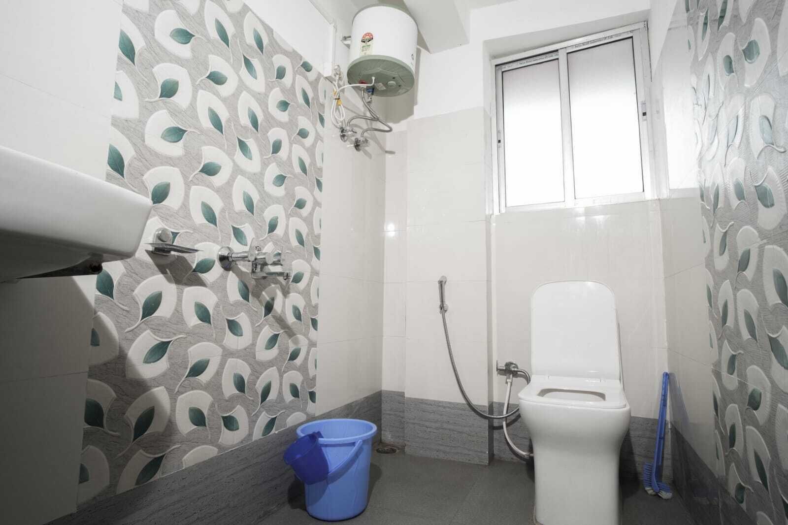 A bathroom with a toilet, shower, and a blue bucket on the floor.