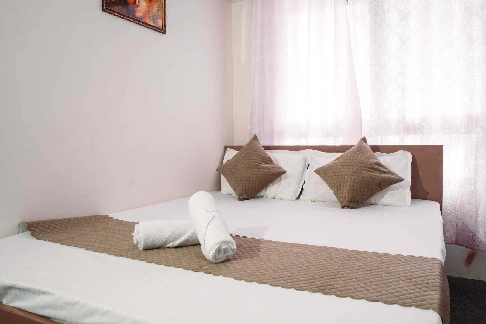 Una cama bien hecha con un edredón marrón acolchado, dos almohadas y una toalla enrollada sobre una colcha blanca.