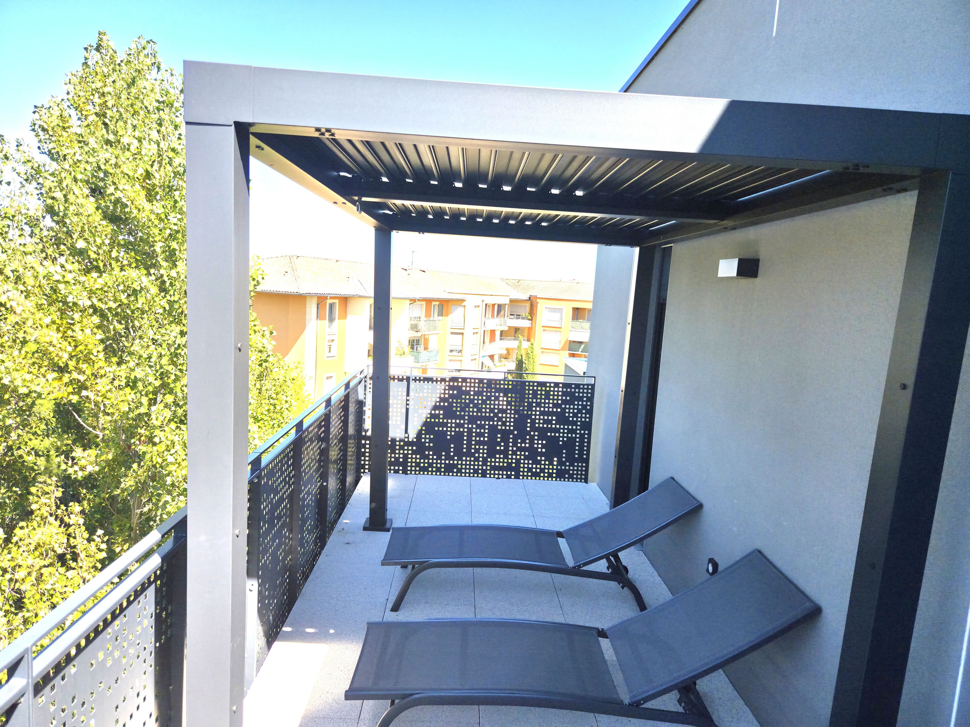 A covered outdoor seating area with metal chairs and a metal fence, overlooking a residential area.