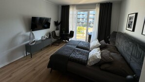 A modern bedroom with a bed, a TV, a seating area, and a balcony view. - Comfortable Apartment, SPA Zone, Dziwnow (Dziwnów)