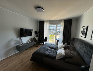 Ein modernes Schlafzimmer mit Bett, Fernseher, einer Sitzecke und Balkonblick.