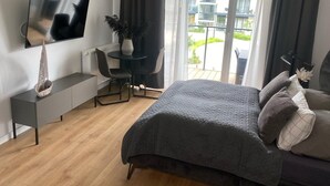 A modern bedroom with a bed, a TV, a desk, and a view of the outside. - Comfortable Apartment, SPA Zone, Dziwnow (Dziwnów)