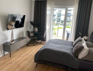 Ein modernes Schlafzimmer mit Bett, Fernseher, Schreibtisch und Blick ins Freie.