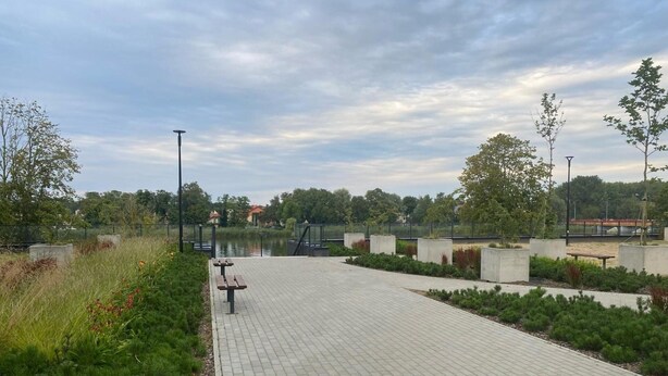 A paved walkway with benches, surrounded by greenery and a body of water. - Comfortable Apartment, SPA Zone, Dziwnow (Dziwnów)