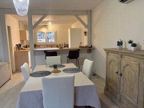 A dining area with a table set for four, chairs, a wooden cabinet, and a kitchen in the background. - Charming renovated Landes house (Mimizan)