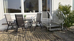 Une terrasse en bois, meublée pour l’extérieur, avec une petite table et des chaises, ainsi qu’une rambarde.