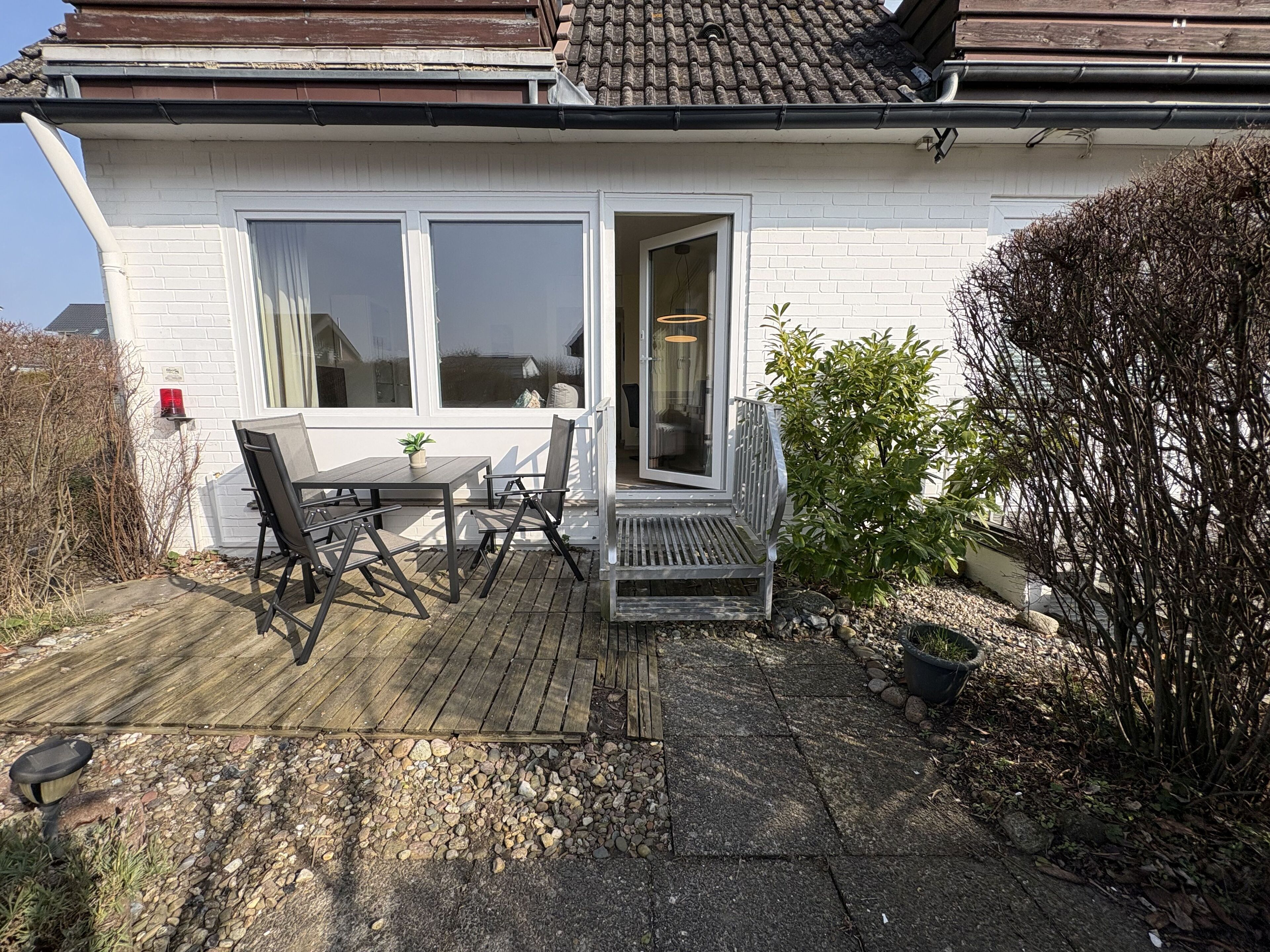 A house with a patio, a table with chairs, a bench, and a potted plant.