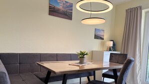 Un espace repas moderne avec une table en bois, des sièges rembourrés, des luminaires suspendus et une plante en pot.