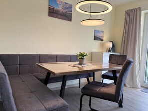 Ein moderner Essbereich mit Holztisch, gepolsterten Sitzmöglichkeiten, Pendelleuchten und einem Blumentopf.