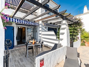 A patio with a table and chairs, a blue door, and a white wall with a sign. - Modern Beachfront Escape, Calahonda (Mijas)