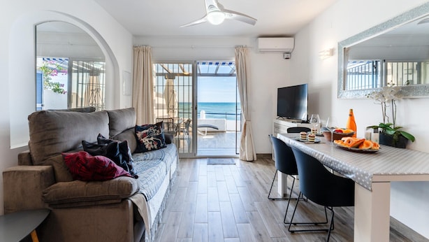 A modern living room with a sofa, a dining table with chairs, a TV, and a view of the sea through a glass door. - Modern Beachfront Escape, Calahonda (Mijas)