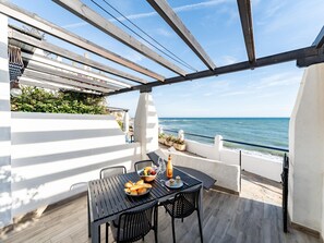 A terrace with a table set for dining, overlooking the sea. - Modern Beachfront Escape, Calahonda (Mijas)