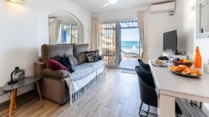 A modern living room with a sofa, a dining table with chairs, a ceiling fan, and a view of the sea. - Modern Beachfront Escape, Calahonda (Mijas)