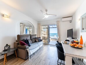 A modern living room with a sofa, a dining table with chairs, a ceiling fan, and a view of the sea. - Modern Beachfront Escape, Calahonda (Mijas)